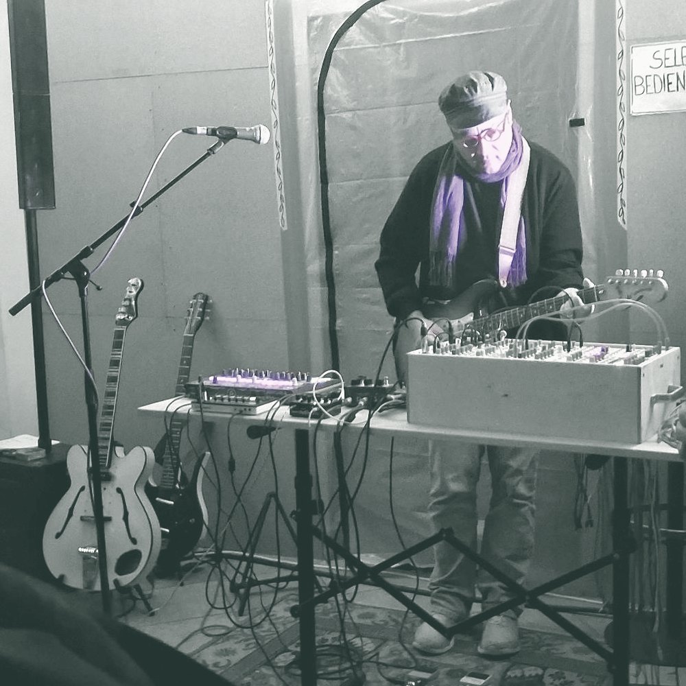 Live set: modular synth, guitar and a drum computer on a table, in front of a microphone